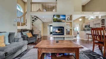 A spacious living area with a fireplace, a dining table, and a kitchen in the background.