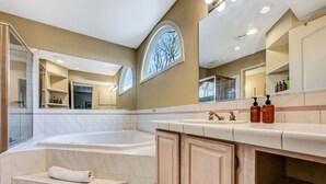 A modern bathroom with a large bathtub, a vanity with a mirror, and a window providing natural light. - Walk 2 Ski: Groups, Kids, Spacious & Well-Stocked (Lake Harmony)