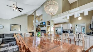 A spacious living area with a wooden dining table, comfortable seating, a chandelier, and a modern kitchen in the background. - Walk 2 Ski: Groups, Kids, Spacious & Well-Stocked (Lake Harmony)