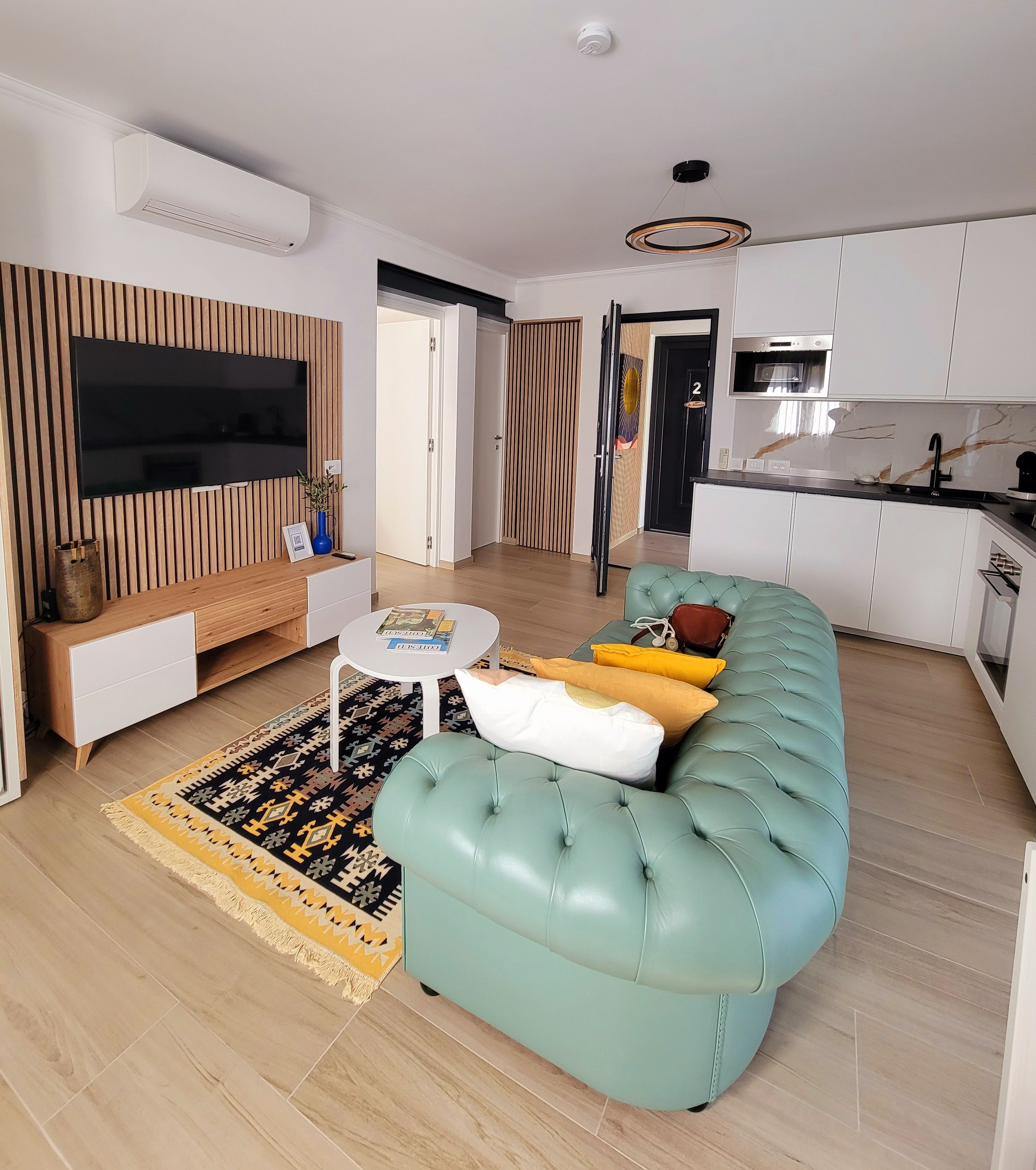 Un salon moderne comprenant un canapé, un téléviseur à écran plat, une petite table basse et un coin cuisine équipé d’un four à micro-ondes.