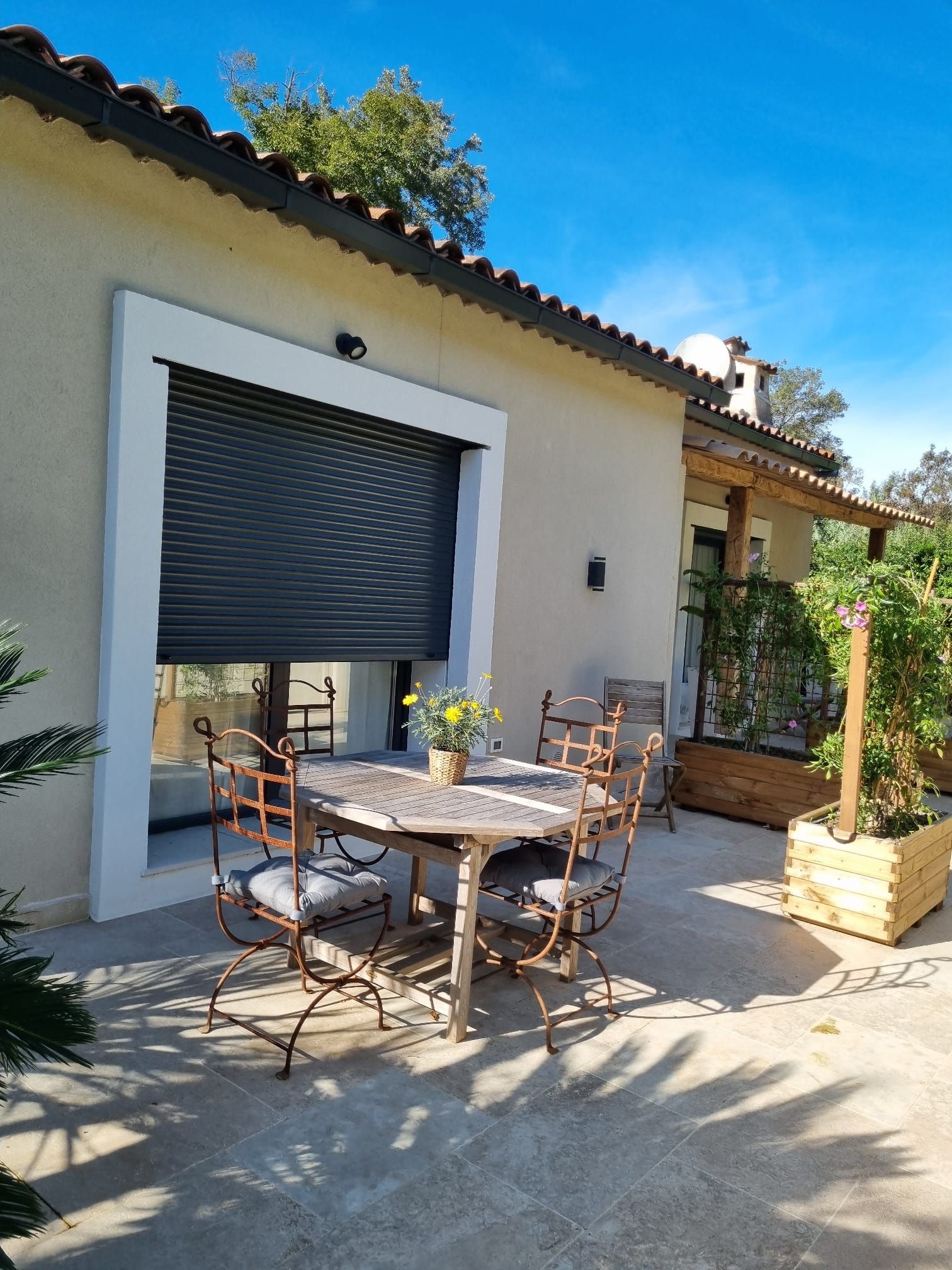 Eine Terrasse im Freien mit Tisch und Stühlen, einem überdachten Bereich und einem Garten.