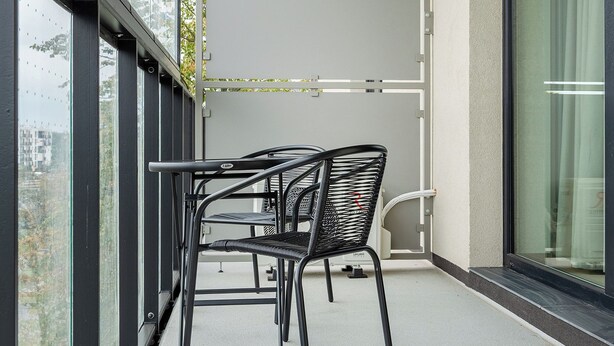 Ein Balkon mit Tisch und Stühlen, ein Fenster mit Blick auf Gebäude und ein Vorhang auf der rechten Seite.