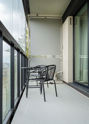 Un balcón con mesa y sillas, una ventana que ofrece vistas a edificios y una cortina a la derecha.