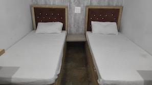 Dos camas individuales con cabeceros de madera y ropa blanca en una habitación estrecha.