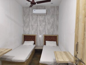 Quarto com duas camas de solteiro, ventilador de teto, ar condicionado e porta de madeira.