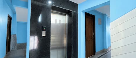 An elevator in a hallway with blue walls and a marble floor.