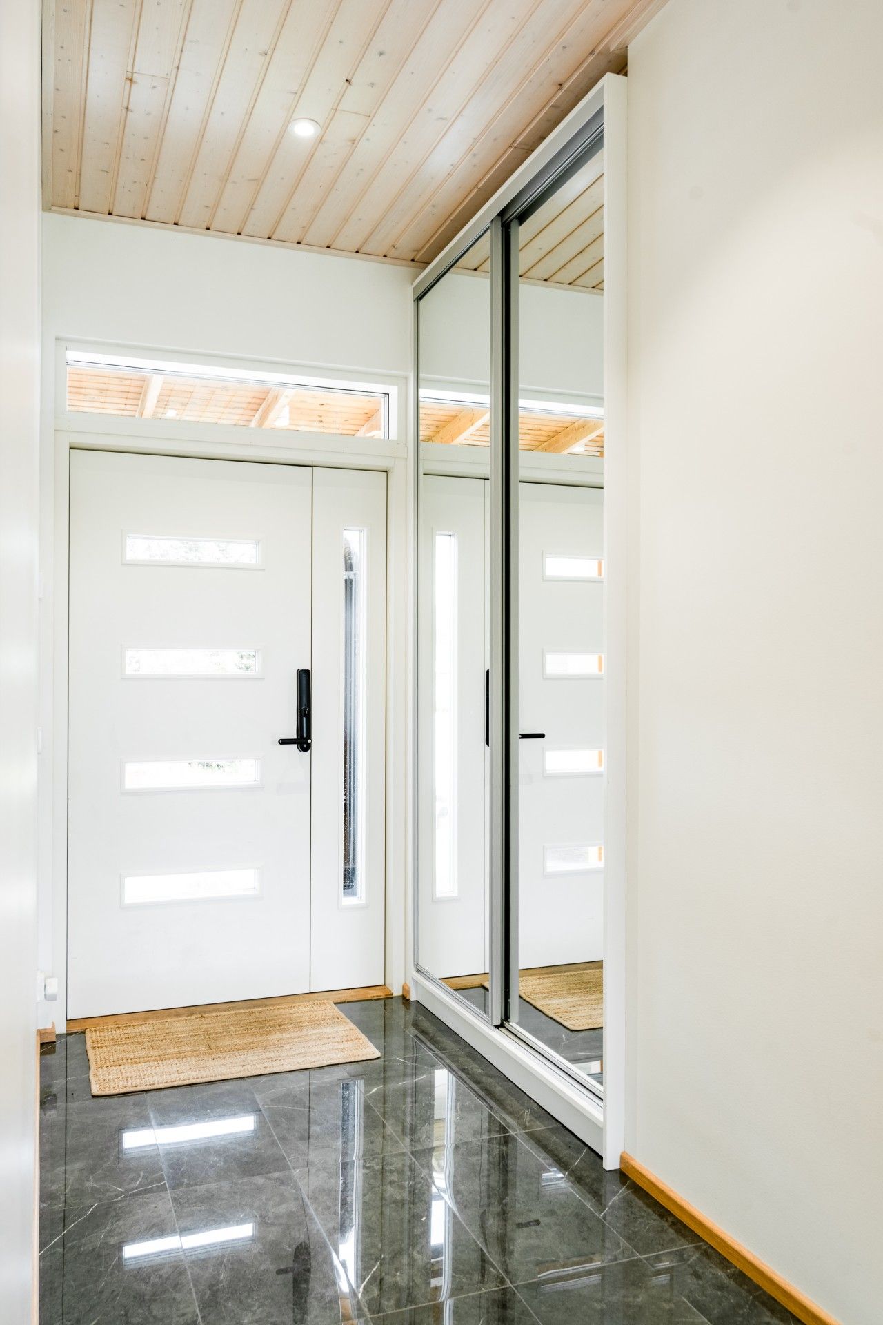 Un couloir doté d’un plancher poli, d’un plafond en bois et d’une porte coulissante en verre.