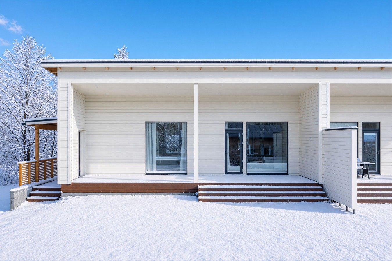 Une maison moderne dotée d’un porche abrité, de grandes fenêtres et surplombant un paysage enneigé.
