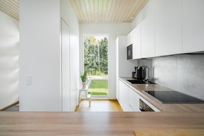 A modern kitchen with white cabinets, a wooden countertop, and a view of a green garden.