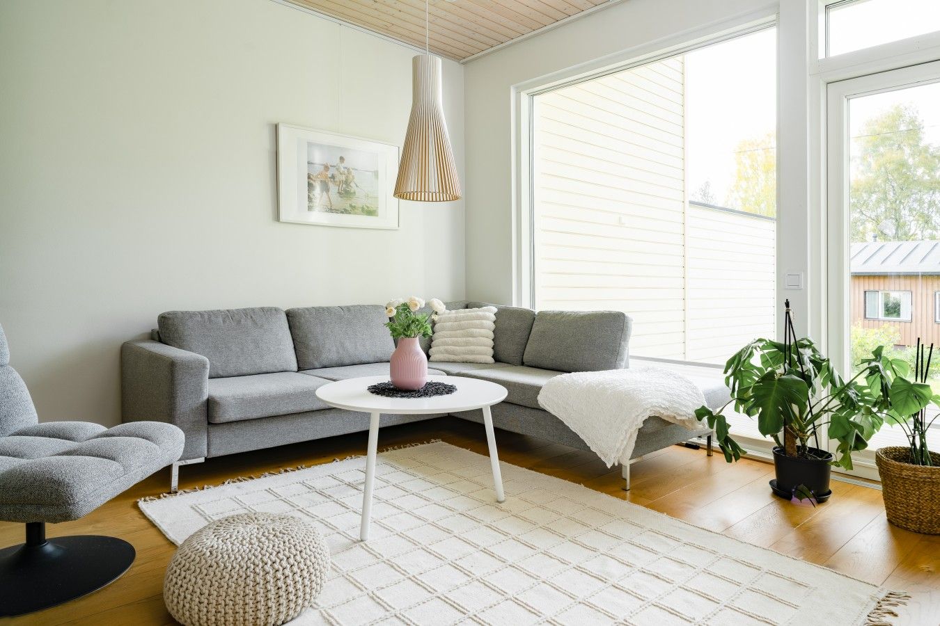 Un salon moderne avec un canapé gris, une table basse ronde, un tapis blanc et une plante en pot.