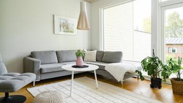 Un salon moderne avec un canapé gris, une table basse ronde, un tapis blanc et une plante en pot.