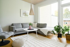 A modern living room with a grey sofa, a round coffee table, a white rug, and a potted plant.
