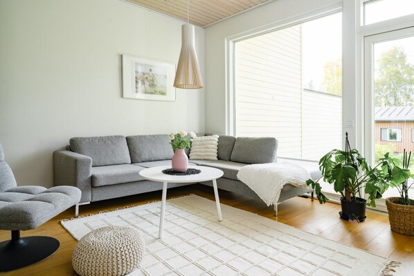 A modern living room with a grey sofa, a round coffee table, a white rug, and a potted plant.
