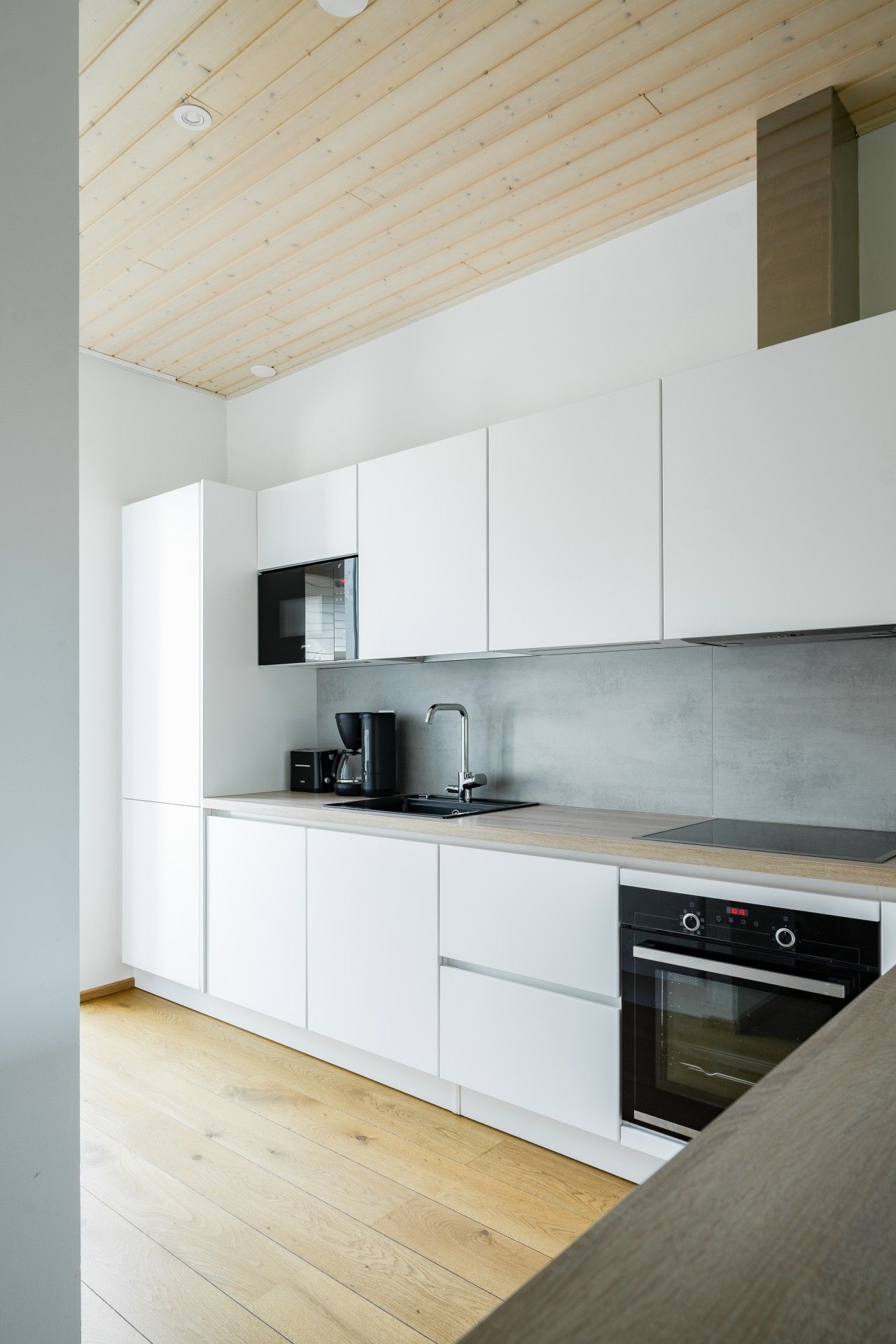 Une cuisine moderne avec des meubles blancs, une cuisinière noire et un plafond en bois.