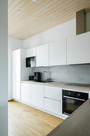 A modern kitchen with white cabinetry, a black stove, and a wooden ceiling. - Santa`s Gateway Home, Sauna By Lapland Host (Rovaniemi)