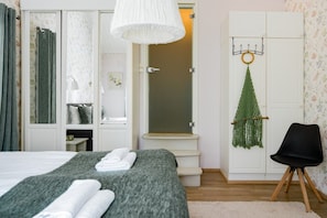 A bedroom with a bed, a chair, a hanging plant, and a door with a mirror.