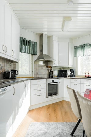 A modern kitchen with white cabinetry, a built-in oven, and a coffee machine.