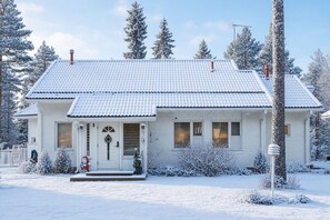 A white house with a tiled roof, surrounded by snow-covered trees and a clear sky.