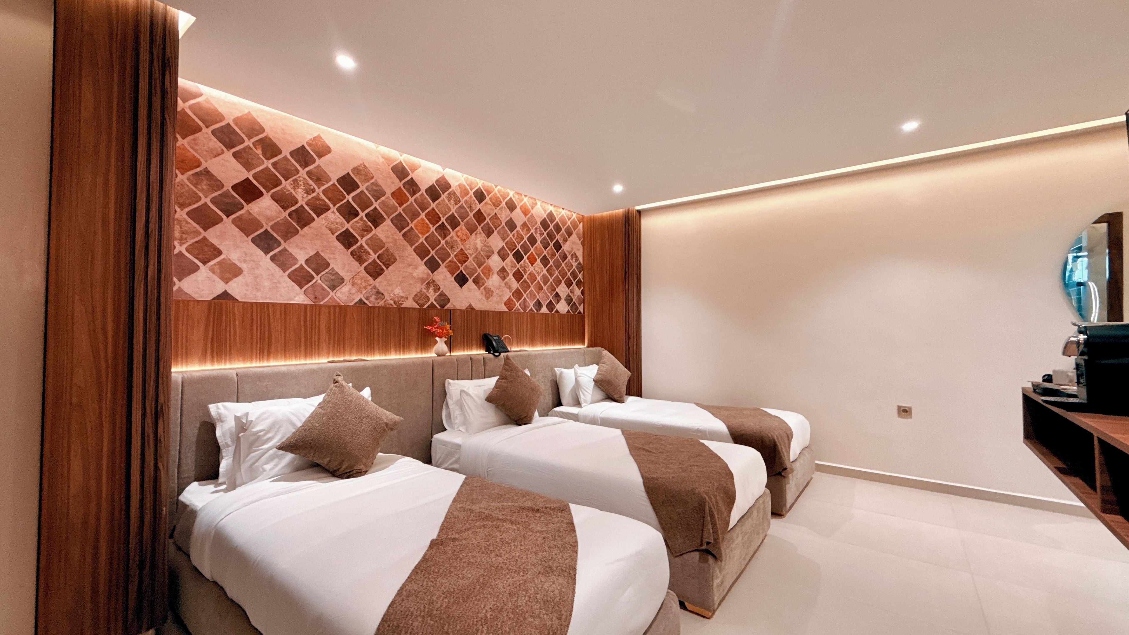 A hotel room with two beds, a wooden headboard, a wall-mounted phone, and a small table with a lamp.