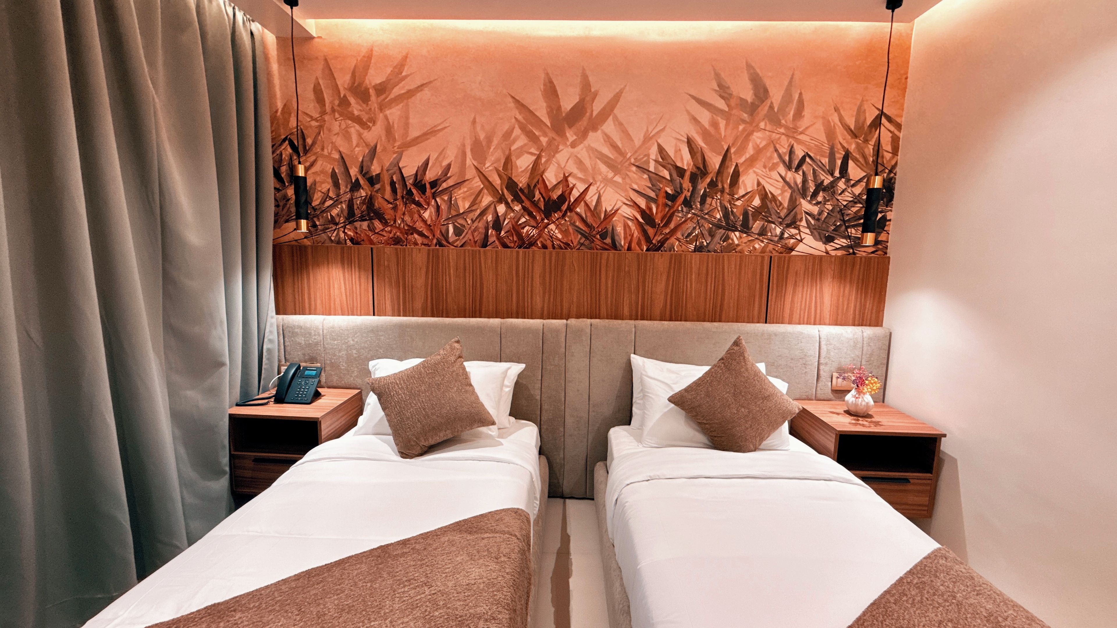 A hotel room with two beds, wooden headboard, bedside tables with lamps, and a wall with a bamboo leaf pattern.