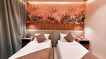 A hotel room with two beds, wooden headboard, bedside tables with lamps, and a wall with a bamboo leaf pattern.