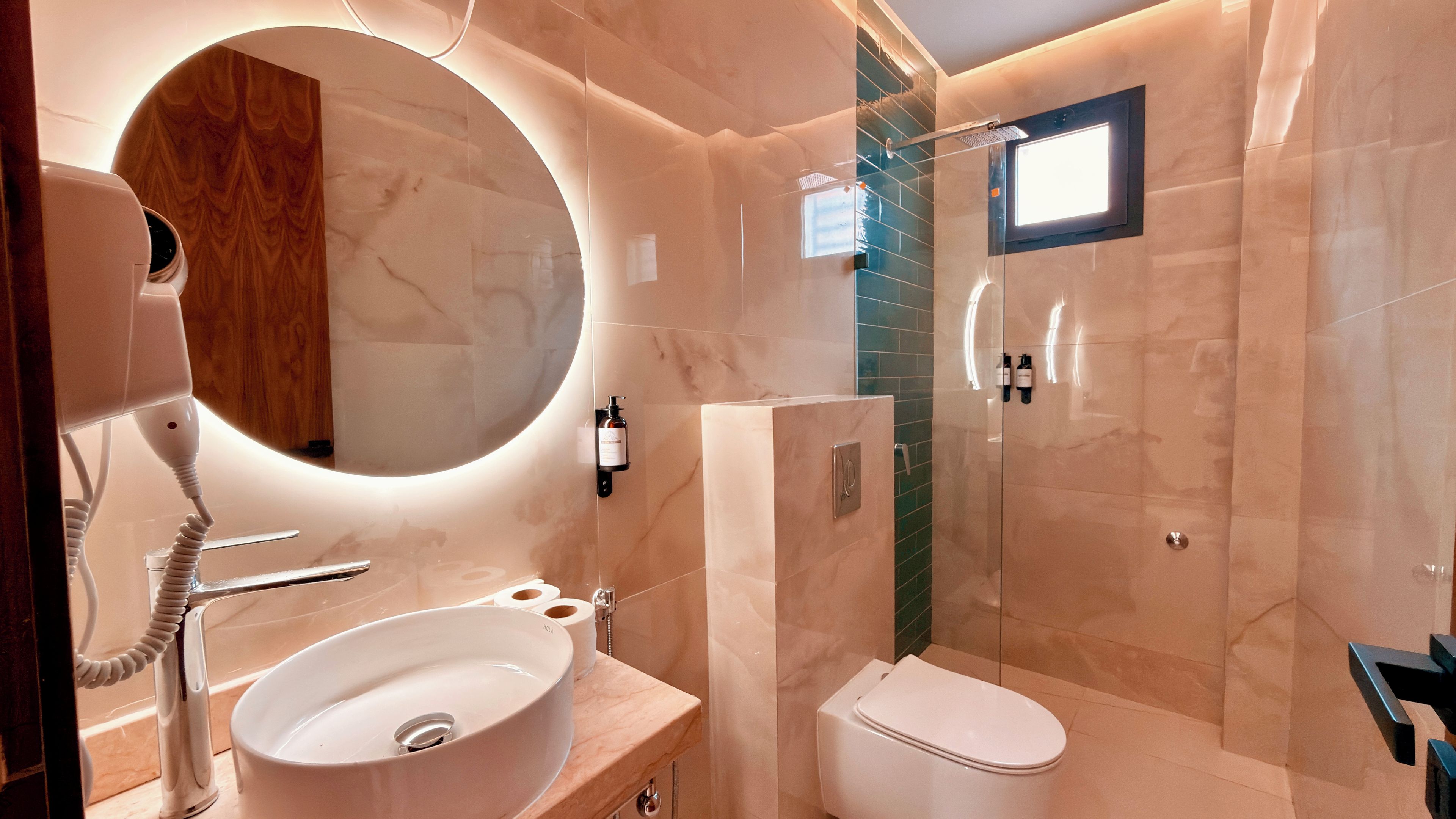 Un baño moderno con un espejo redondo, un lavabo, un inodoro y una zona de ducha.
