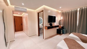 Une chambre d’hôtel avec un lit, un bureau doté d’un téléviseur à écran plat, un miroir et une salle de bain visible à travers une porte ouverte.