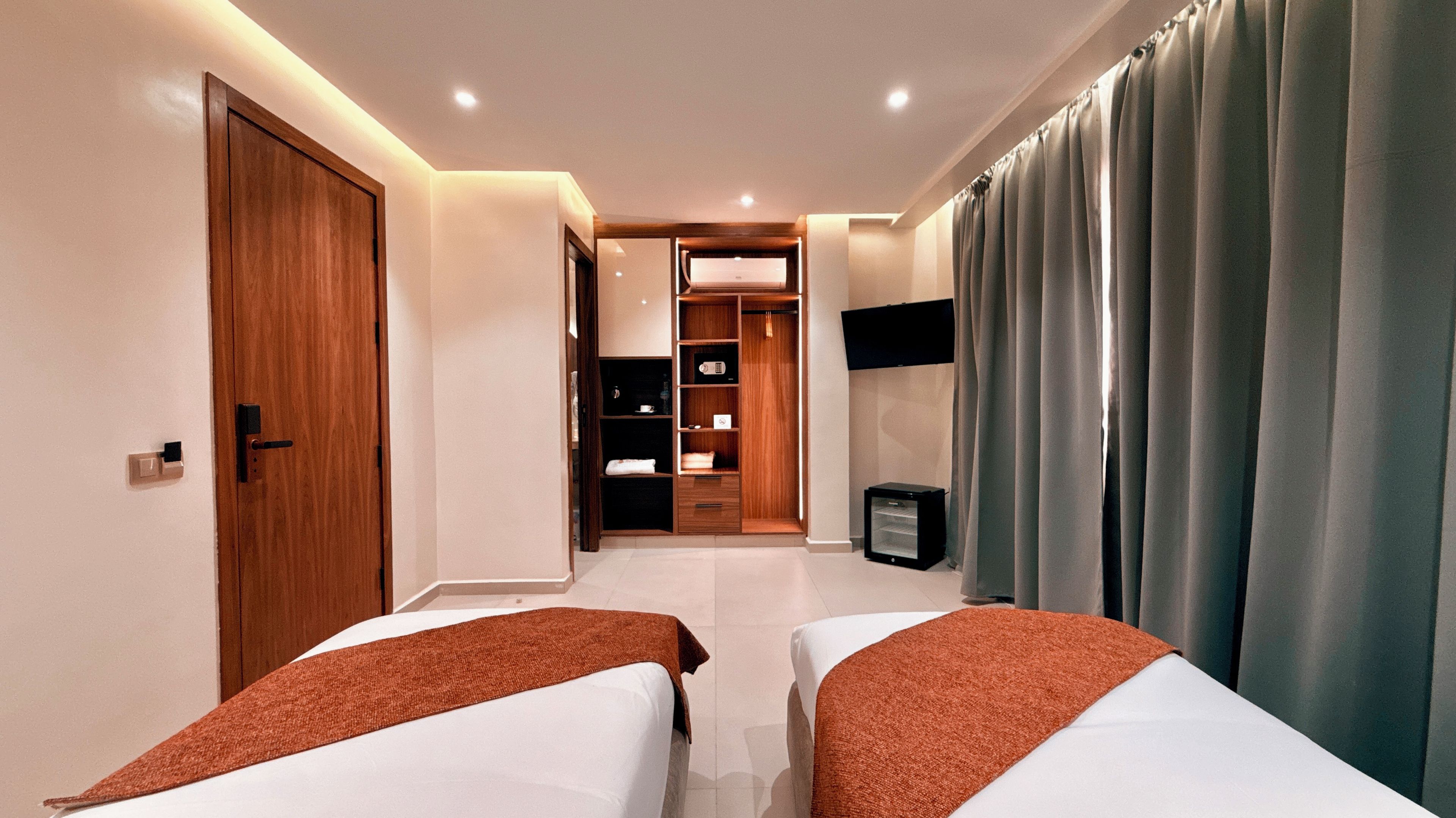 Une chambre d’hôtel avec deux lits, une armoire, un téléviseur et une salle de bain que l’on aperçoit à l’arrière-plan.