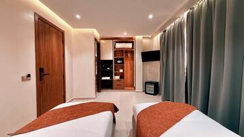 Une chambre d’hôtel avec deux lits, une armoire, un téléviseur et une salle de bain que l’on aperçoit à l’arrière-plan.