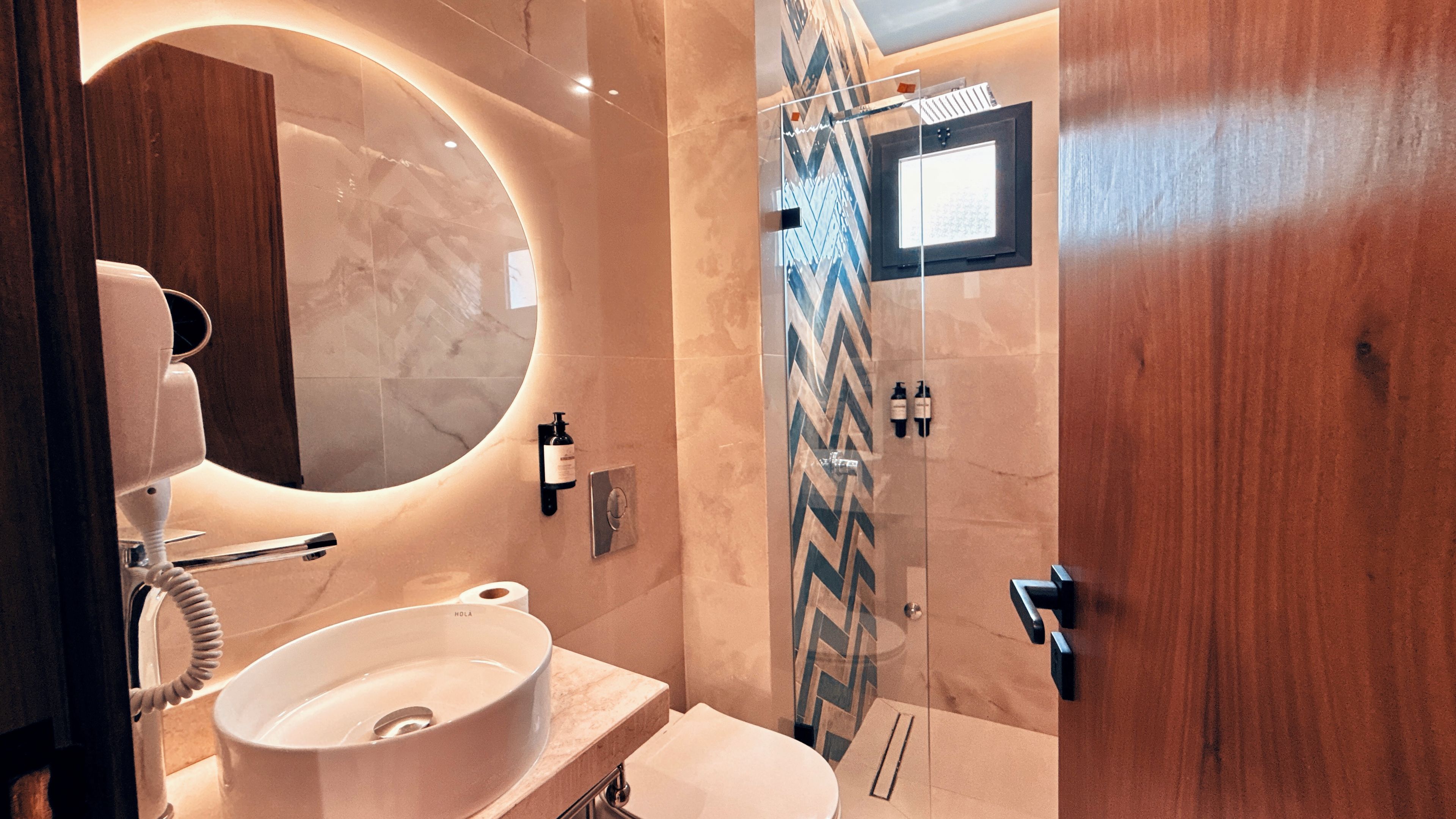 A bathroom with a round mirror, a sink, a toilet, and a shower area.