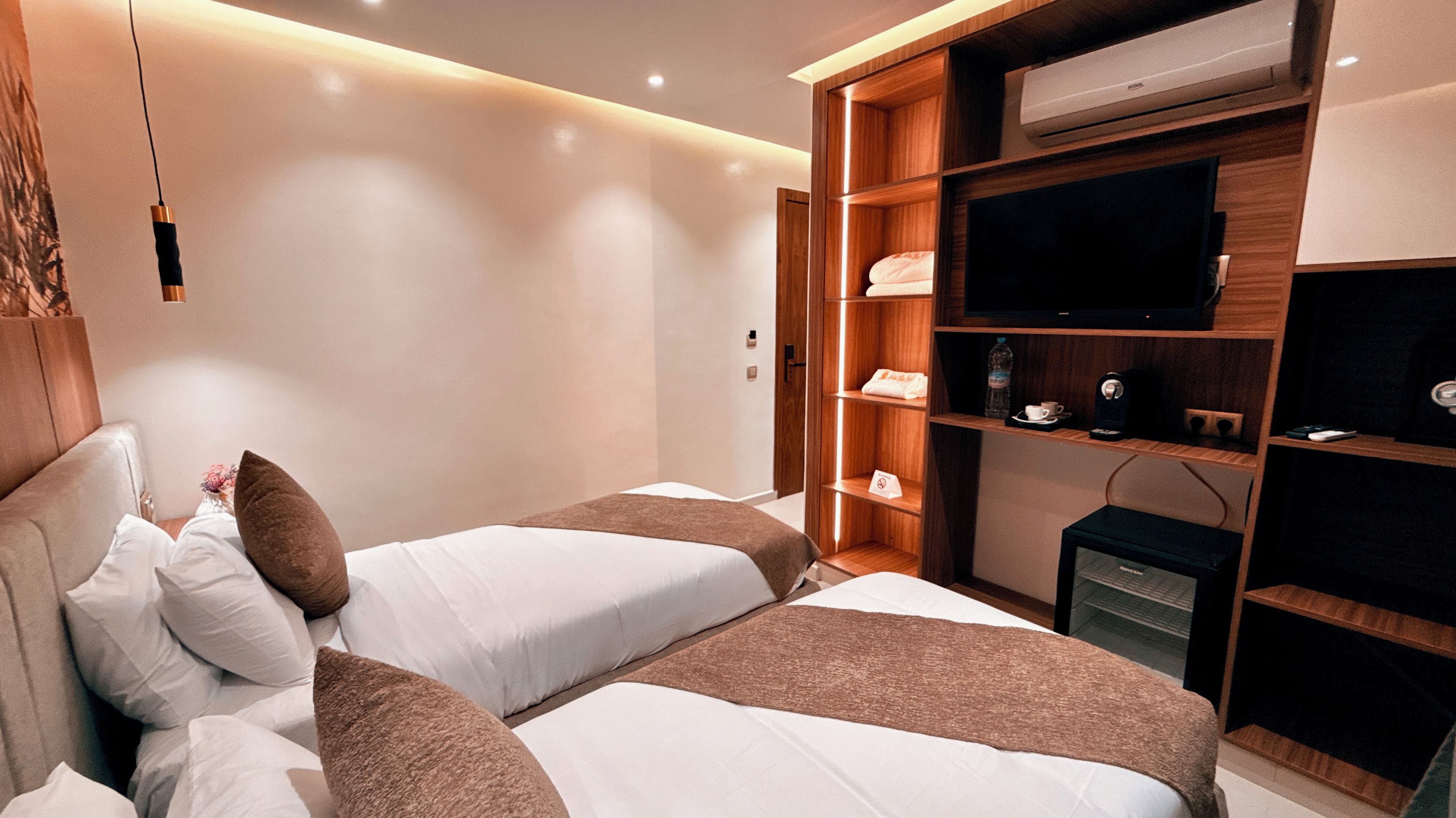 Habitación de hotel con dos camas, televisión, minibar y armario de madera.