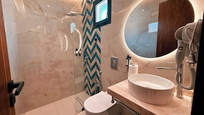 Et moderne badeværelse med et stort spejl, en rund vask og en bruseniche med et chevron-mønstret vægdesign.