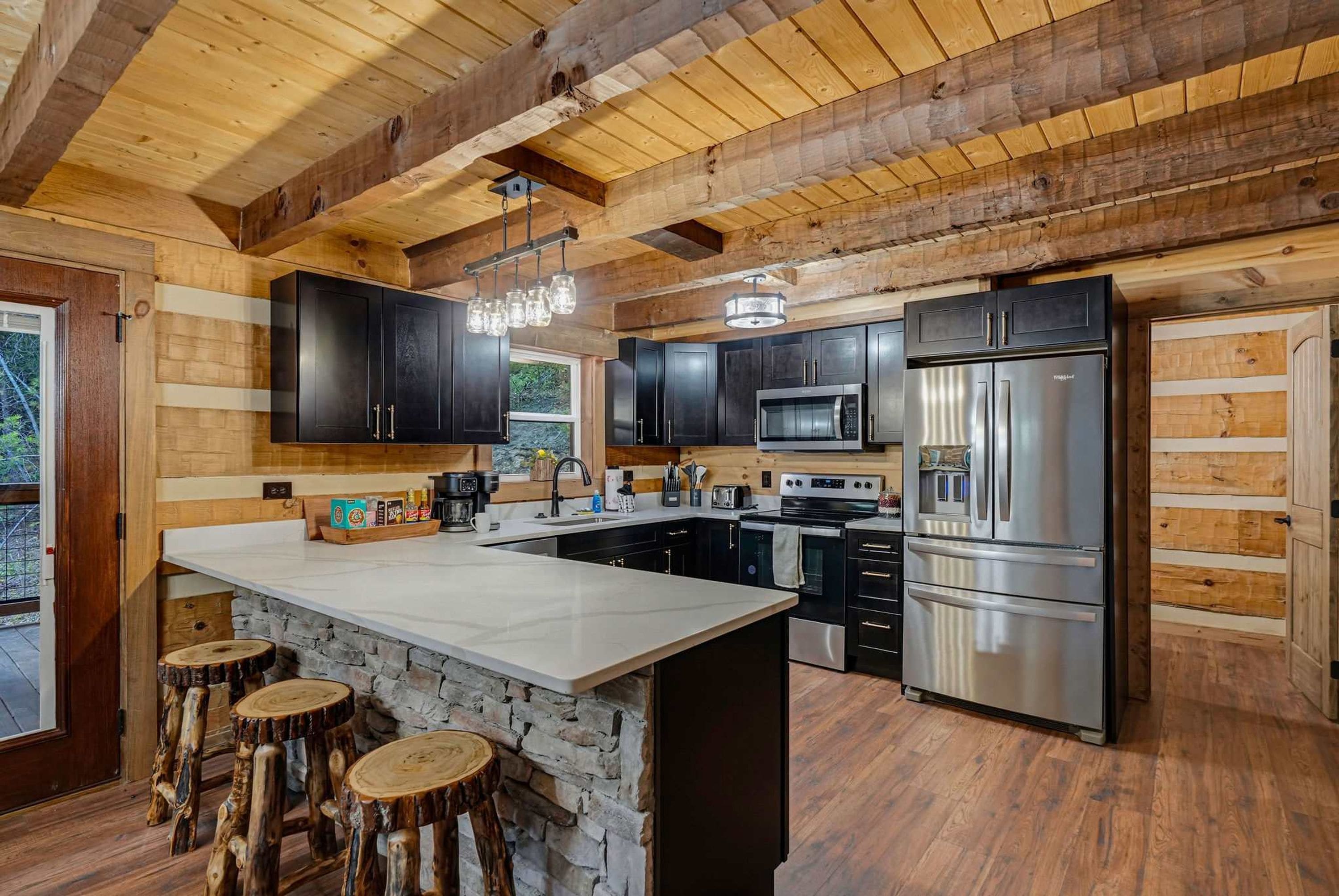 A kitchen with a central island, black cabinets, stainless steel appliances, and a stone accent wall.