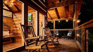 A wooden cabin interior with a porch featuring rustic wooden chairs and a stone fireplace. - Black Bear Ln in Sevierville (Sevierville)