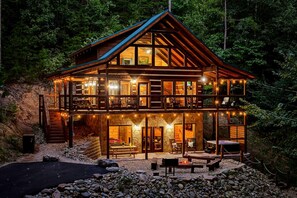 Eine zweistöckige Holzhütte mit Balkon, Steinmauern und Feuerstelle.