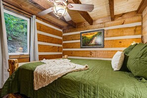 Ein Schlafzimmer in einer Holzhütte mit einem Bett, einem gerahmten Bild von Laurel Falls und einem Deckenventilator.