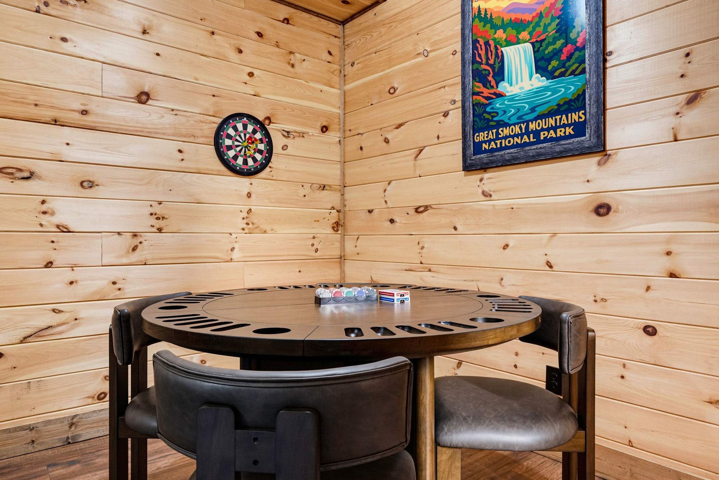 Ein Holzinnenraum mit Dartscheibe, einem Poster vom Great Smoky Mountains National Park und einem runden Tisch mit Stühlen.