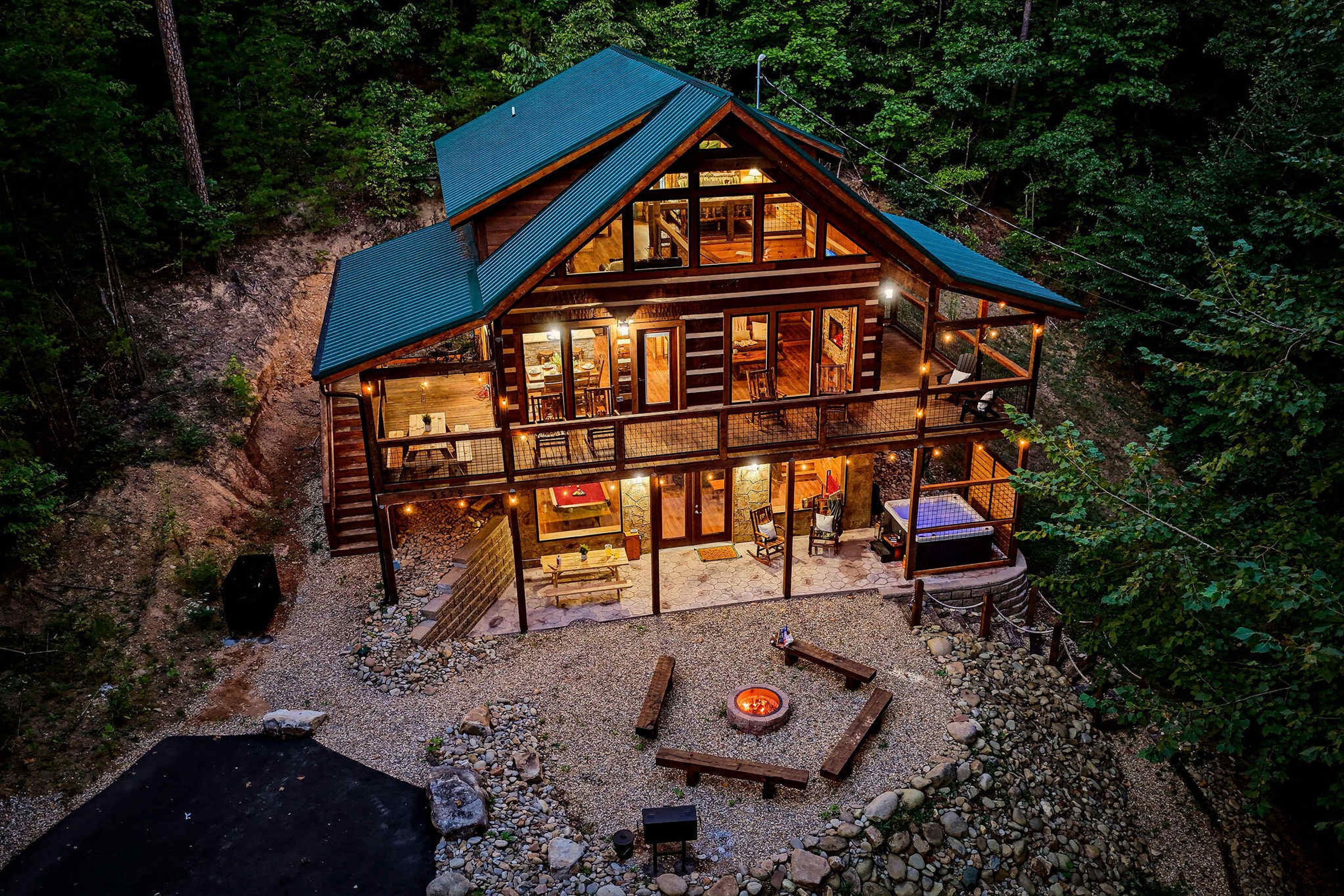 A two-story log cabin with a stone fireplace, outdoor seating, and a deck.