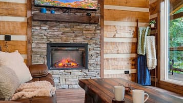 A cozy living room with a stone fireplace, wooden walls, a comfortable sofa, and a coffee table.