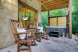 A stone-walled outdoor seating area with wooden chairs and a bench, a hot tub, and a view of a forested area. - Black Bear Ln in Sevierville (Sevierville)