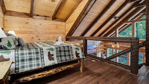 A cozy cabin room with a wooden ceiling, a bed with a plaid bedspread, and a view of a wooden deck outside. - Black Bear Ln in Sevierville (Sevierville)