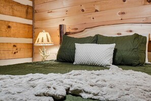 Una habitación tipo cabaña de madera con una cama, una lámpara y una manta.