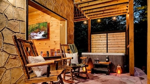 A cozy outdoor seating area with wooden chairs and a table, a stone wall, and a large window with a view of the night sky. - Black Bear Ln in Sevierville (Sevierville)