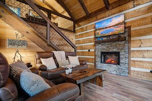 Interior acogedor de una cabaña de troncos con chimenea de piedra, sofá de cuero y televisor grande montado en la pared.