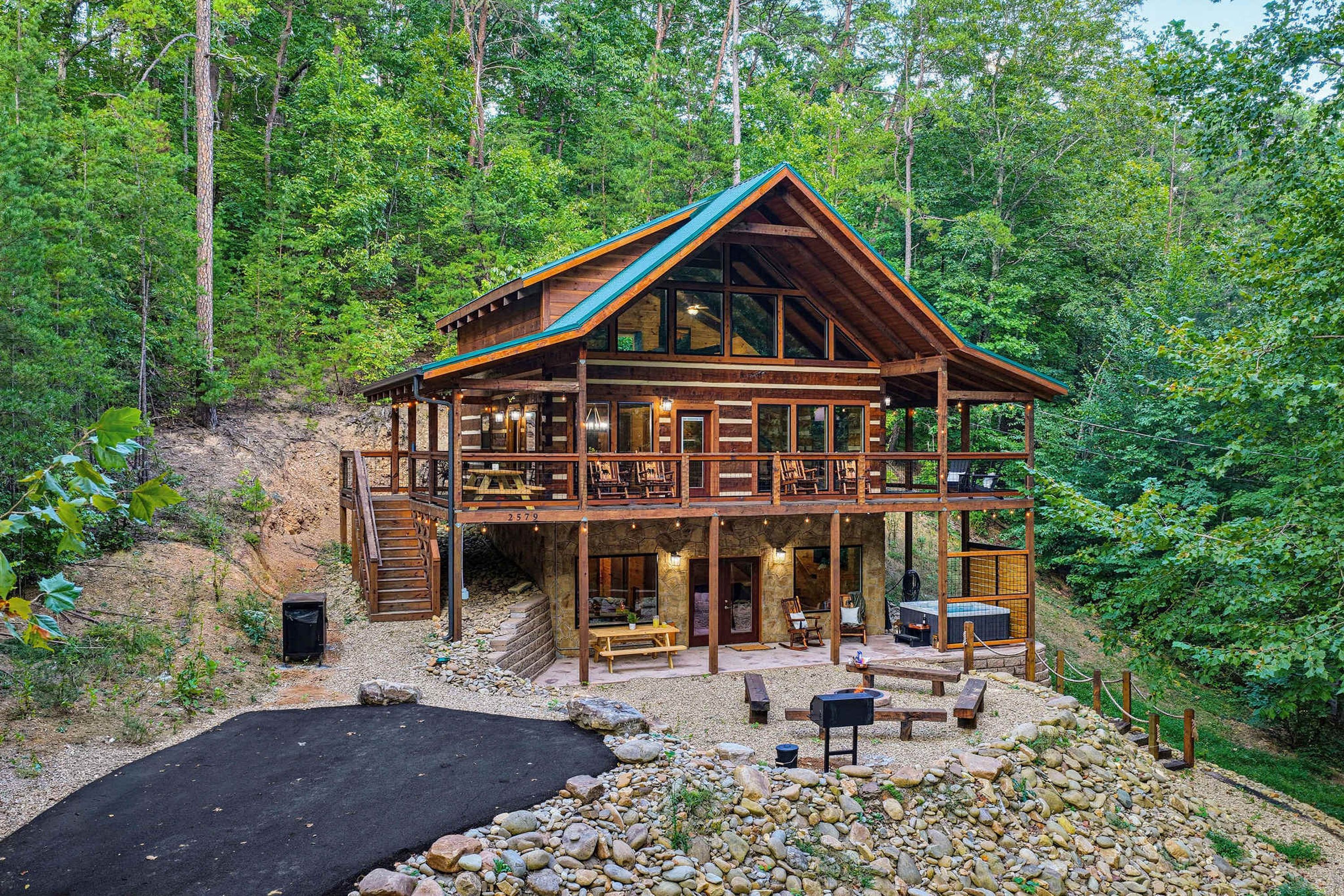 Une cabane en rondins à deux étages, dotée d’un balcon, d’un espace salon extérieur et d’une cheminée en pierre.