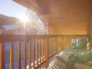 Eine Holzterrasse mit Geländer, einem Stuhl und Blick auf Häuser im Hintergrund.