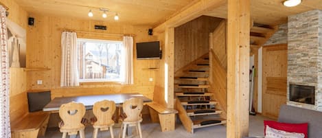 A wooden interior with a dining area, a staircase, and a stone fireplace.