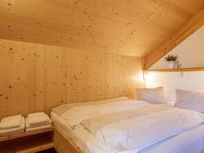 Ein Zimmer aus Holz mit einem Bett, Kissen und einem Regal mit gefalteten Handtüchern.