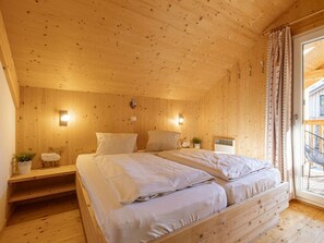 A wooden cabin bedroom with a bed, bedside tables, and a window with curtains. - One-bedroom Cabin (Sankt Georgen am Kreischberg)