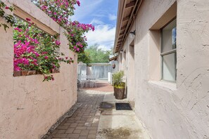 A narrow alleyway with a brick pathway, a white metal table and chairs, and a potted plant. - Great Walkable Location! Tucson Studio Stay (Tucson)
